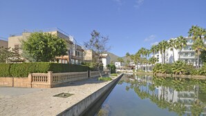 Ein Kanal mit Steinweg, Palmen und modernen Gebäuden im Hintergrund.