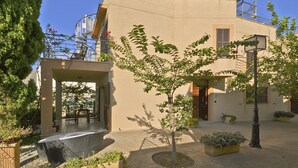 Ein Gebäude mit einer überdachten Terrasse, einem kleinen Baum und Topfpflanzen.