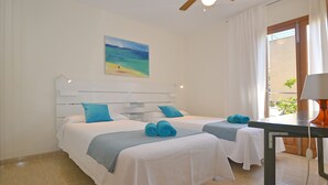 Ein Hotelzimmer mit zwei Betten, einem Deckenventilator, einem Strandbild und einem Fenster mit Vorhängen.