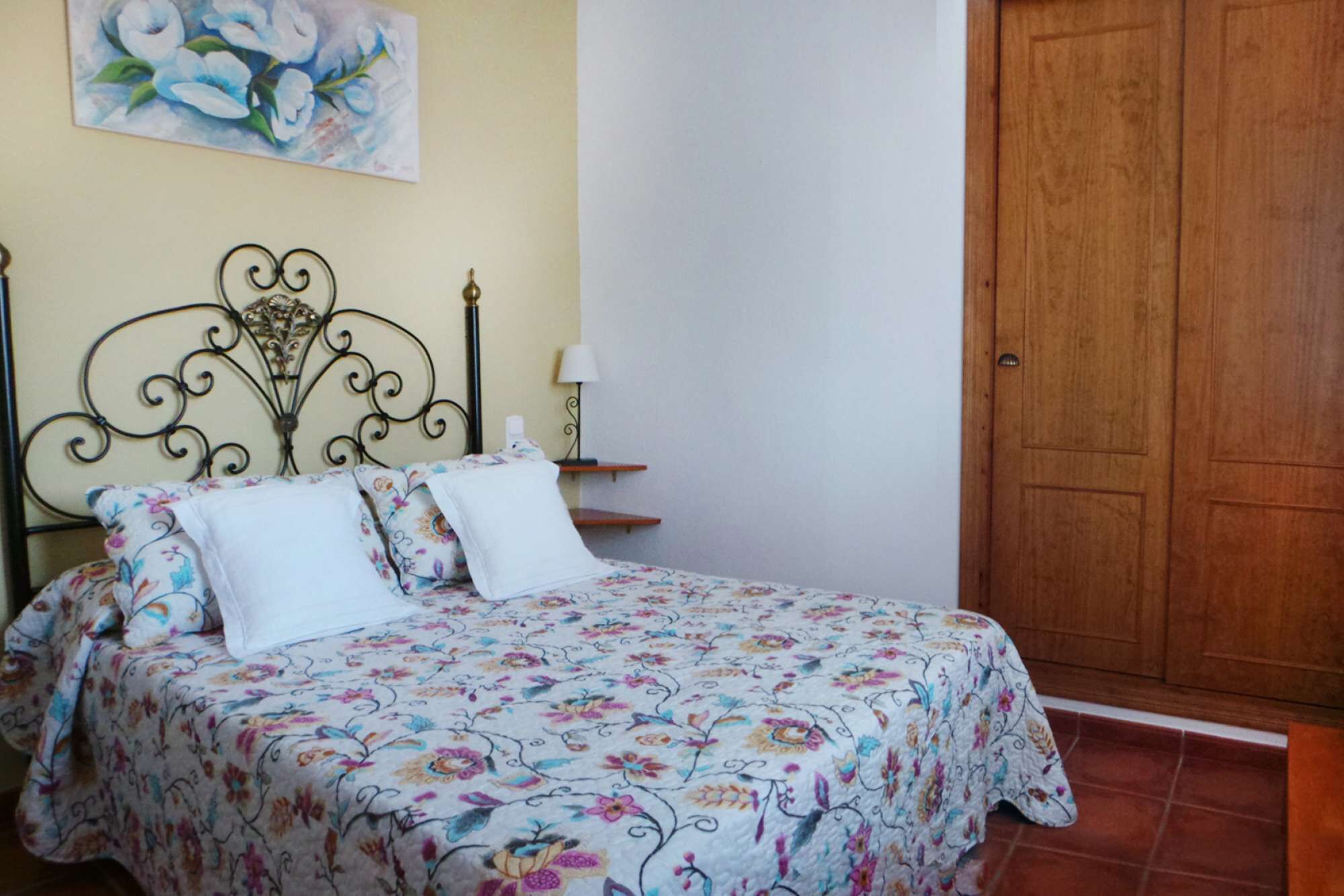 A bed with a floral bedspread, a nightstand with a lamp, and a wooden door.