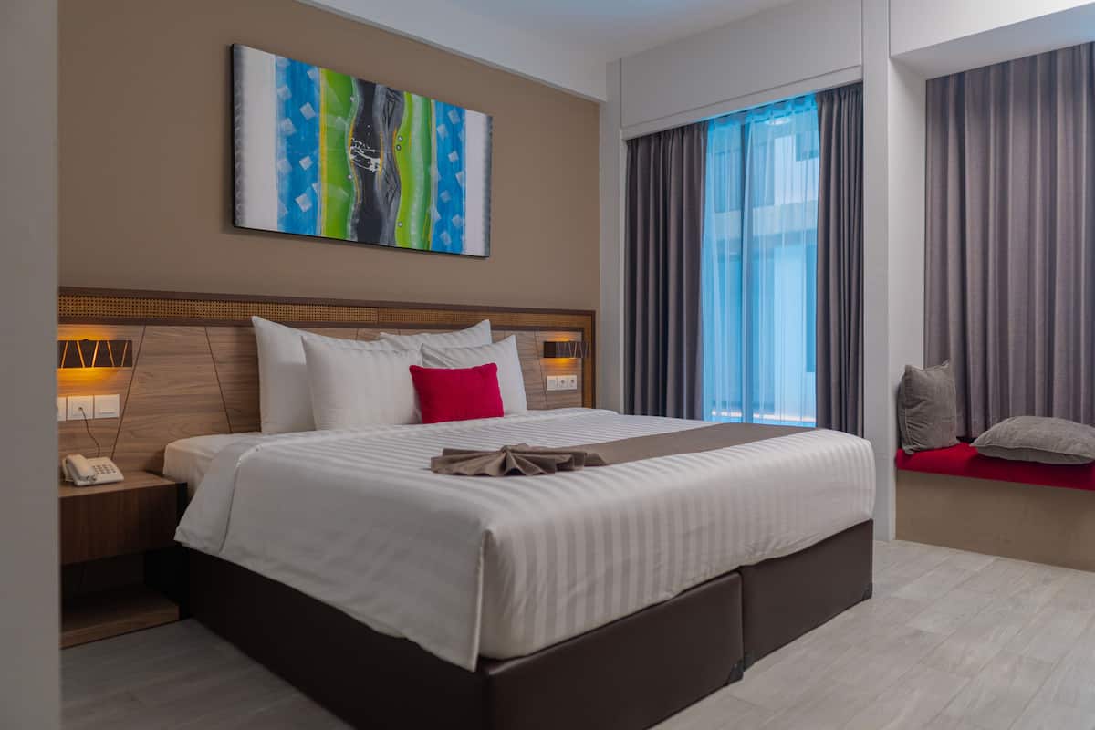 Ein modernes Hotelzimmer mit einem großen Bett, einem Nachttisch mit Lampe, einem Telefon und einem farbenfrohen, abstrakten Gemälde an der Wand.
