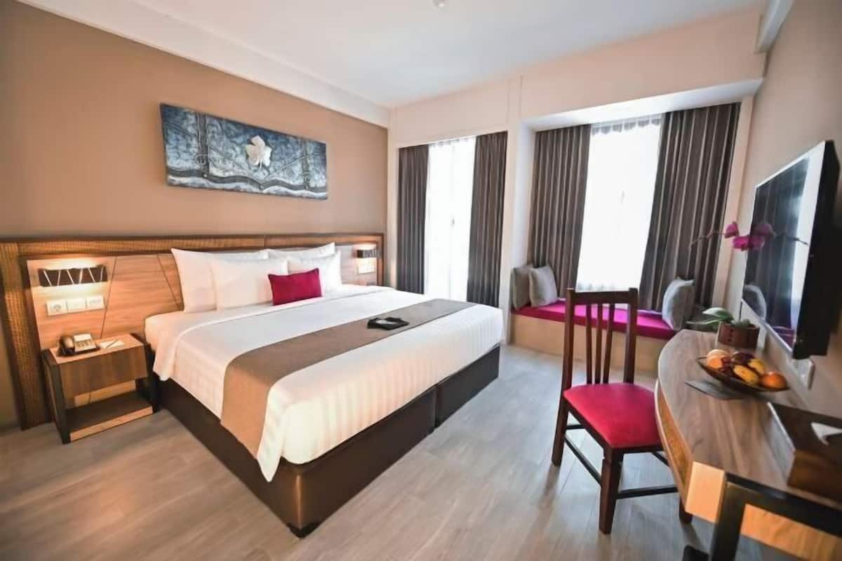 Ein Hotelzimmer mit einem großen Bett, Nachttischen, einem Schreibtisch mit Stuhl, einem Fernseher und einem Fenster mit Vorhängen.