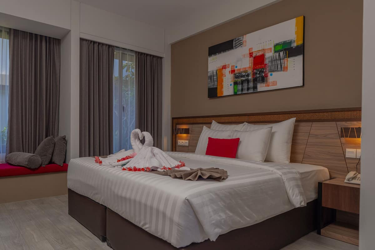 Ein Hotelzimmer mit einem großen Bett, einem Nachttisch mit Telefon, einem an der Wand hängenden abstrakten Gemälde und einem Fenster mit Vorhängen.