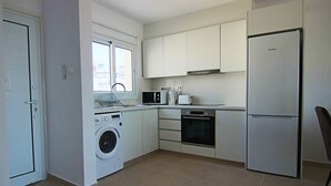 A compact kitchen with a washing machine, microwave, oven, and refrigerator. - Phaedrus Living: Seaview Luxury Flat Limnaria 151 (Paphos)