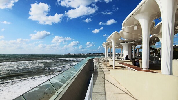 A seaside promenade with a glass balustrade overlooking the ocean, white columns, and outdoor seating areas. - Phaedrus Living: Seaview Luxury Flat Limnaria 151 (Paphos)