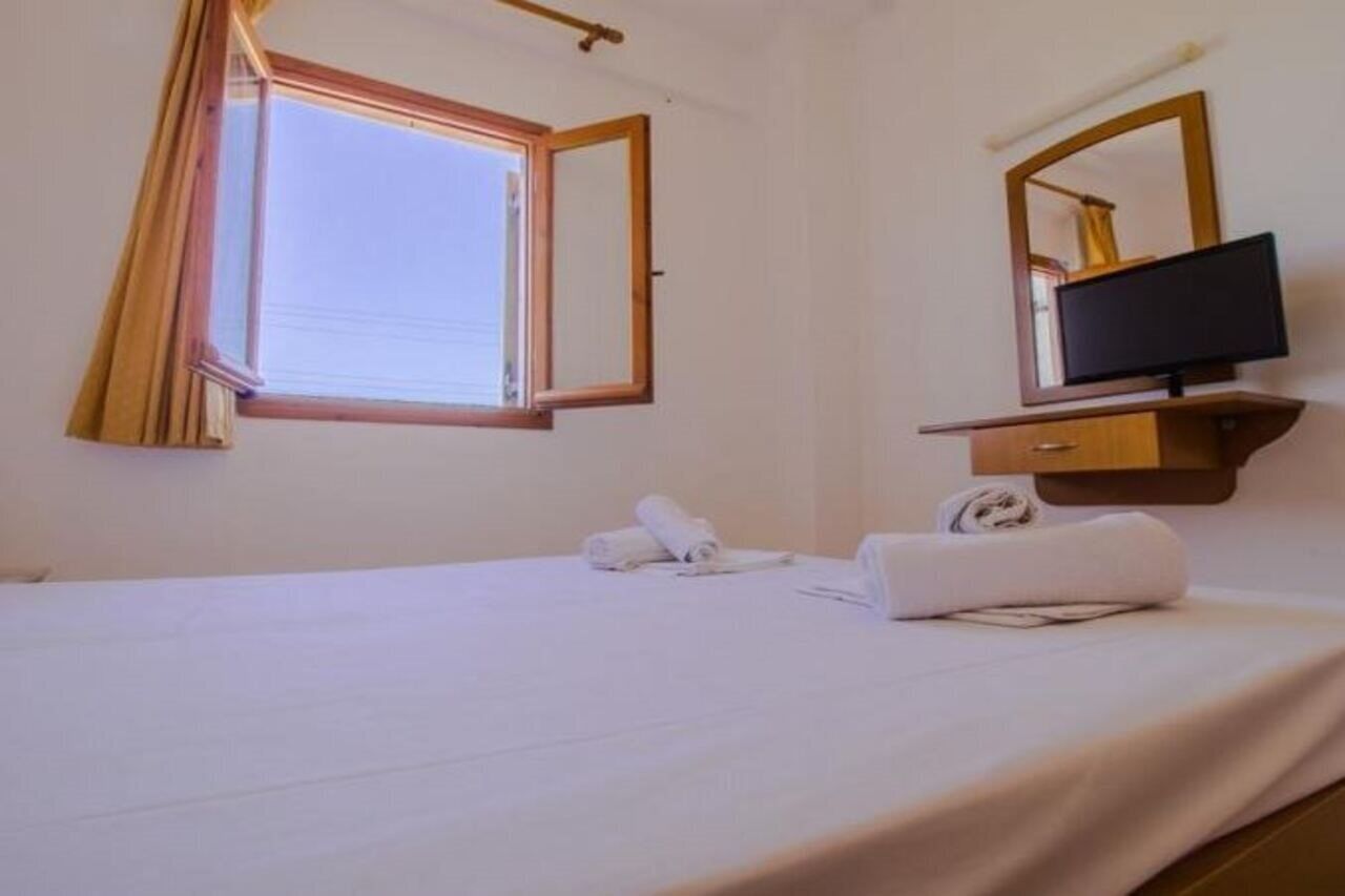 A hotel room with a bed, a television on a wooden stand, a window with curtains, and a mirror.