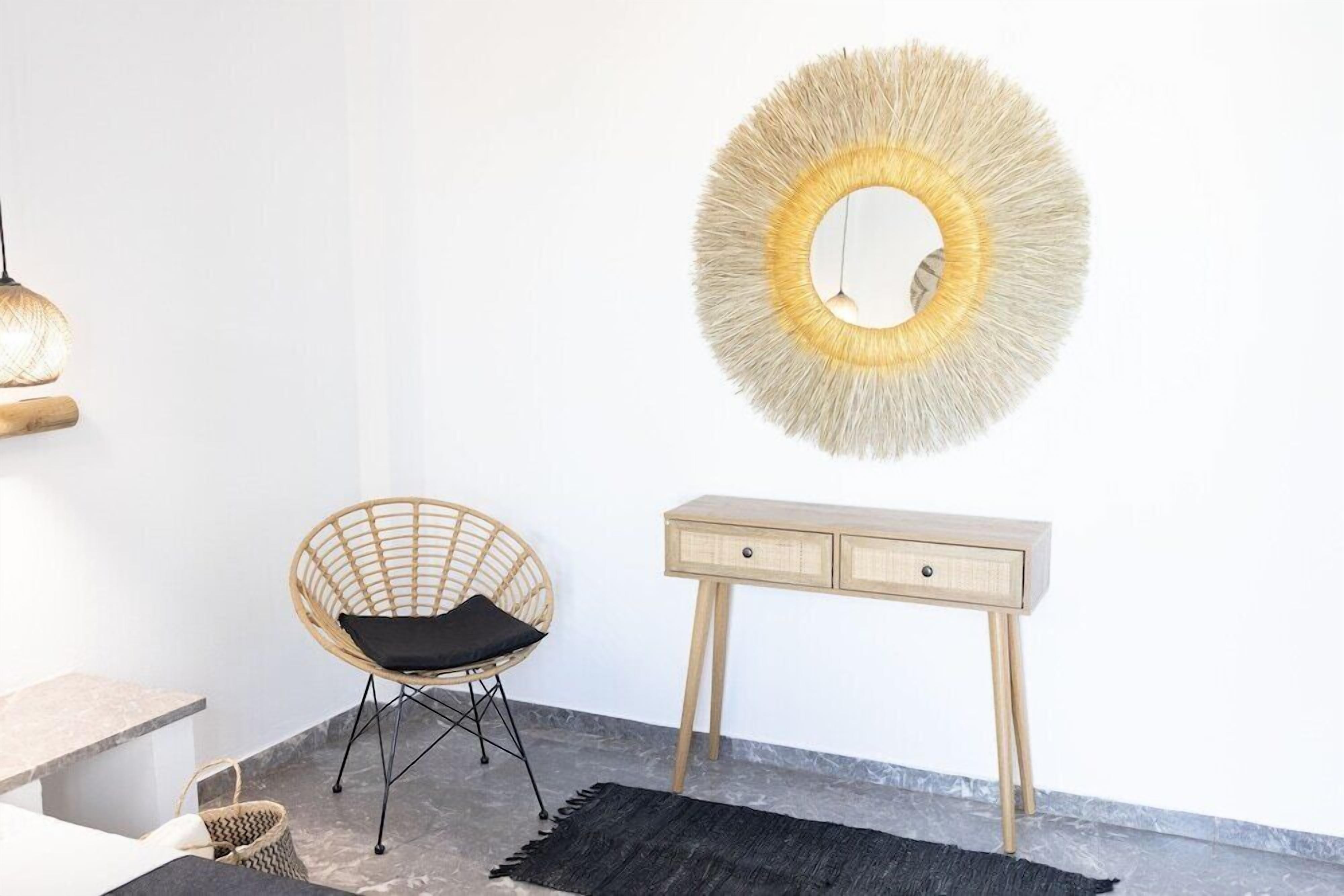 A room with a woven chair, a wooden console table, a round mirror, and a hanging light fixture.