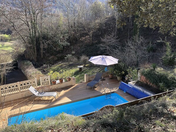 A backyard with a swimming pool, a patio with a table and chairs, and a large umbrella.