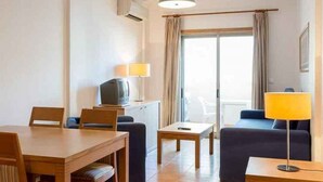 Habitación de hotel con mesa de comedor, sillas, sofá, televisor y lámpara.