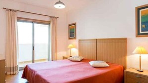 Habitación de hotel con cama, dos lámparas de noche, una ventana con cortinas y un cuadro en la pared.