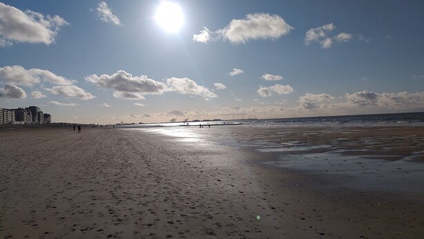A beach with footprints, a pier in the distance, and buildings on the left.
