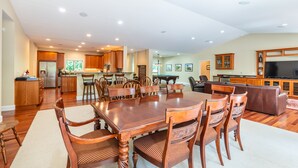 A spacious living area with a large wooden dining table surrounded by chairs, a kitchen with wooden cabinets, and a seating area with a sofa and TV. - Spectacular Golf Group Vacation Rental at Bandon Dunes Golf Resort (Bandon)