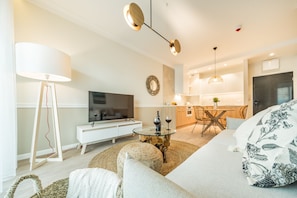 A modern living room with a sofa, a glass coffee table, a TV, and a dining area with a table and chairs.