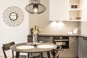 A modern kitchen with a round dining table, two chairs, a vase with flowers, a coffee maker, and a built-in oven.