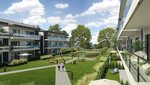 A modern building with multiple balconies, a grassy courtyard with seating, and a clear view of the sky. - Rezydencja Niechorze (Rewal)