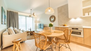A modern living room with a sofa, dining table, and wicker chairs. There is a kitchen area with a stove and cabinets. - Rezydencja Niechorze (Rewal)