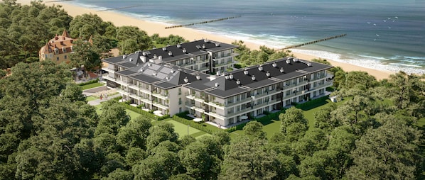 A modern multi-story building with a flat roof, surrounded by dense greenery and a beach.