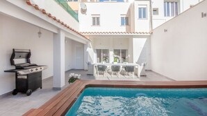 Un área junto a la piscina con una parrilla, una mesa de comedor con sillas y vistas del edificio al fondo.
