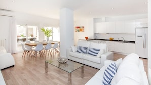 Una sala de estar moderna con una mesa de centro de vidrio, sofás blancos y una zona de comedor con mesa y sillas.