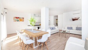 Una sala moderna con una mesa de comedor de madera, sillas blancas, una mesa de centro de vidrio y un sofá blanco con almohadones a rayas.