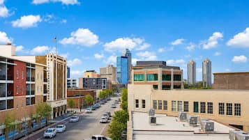 A cityscape with a clear sky, a mix of modern and older buildings, and a street lined with parked cars.