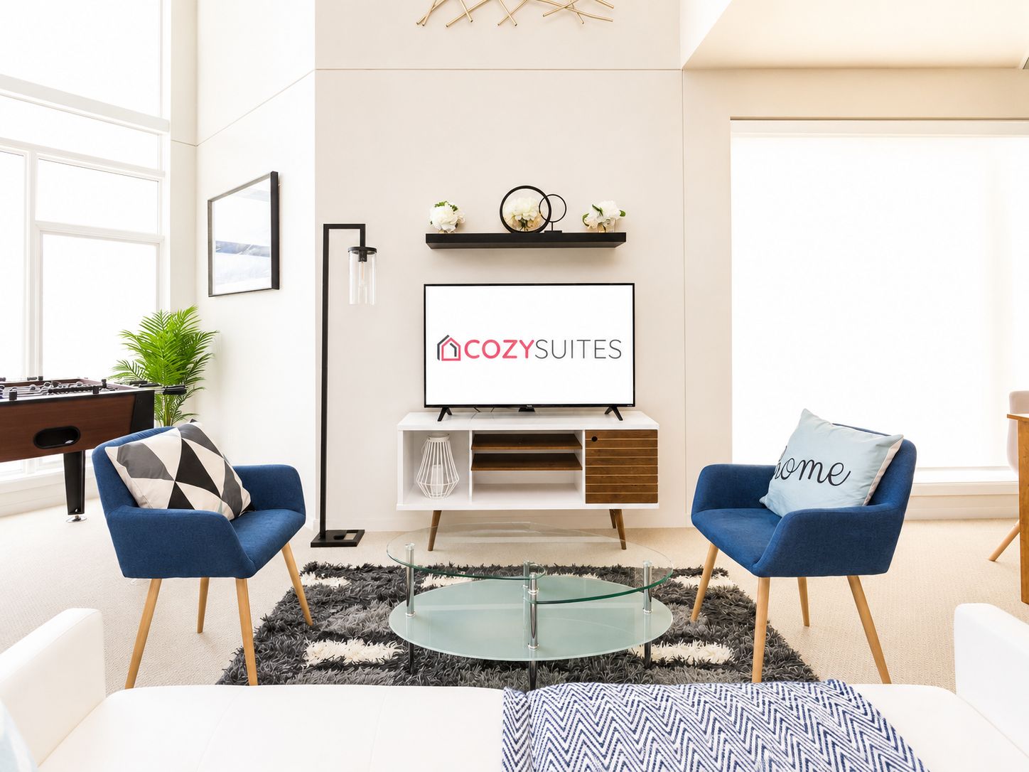 Una sala de estar moderna con un sofá, una mesa de centro y un televisor de pantalla plana mostrando el logotipo de 'COZY SUITES'.