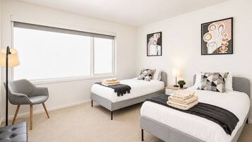 A hotel room with two beds, a chair, a lamp, and artwork on the walls.