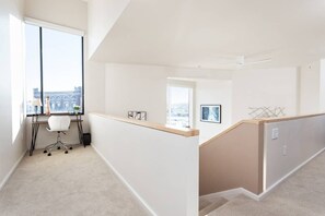 Un appartement moderne doté d’une grande fenêtre, d’un bureau et offrant une vue sur le paysage urbain.