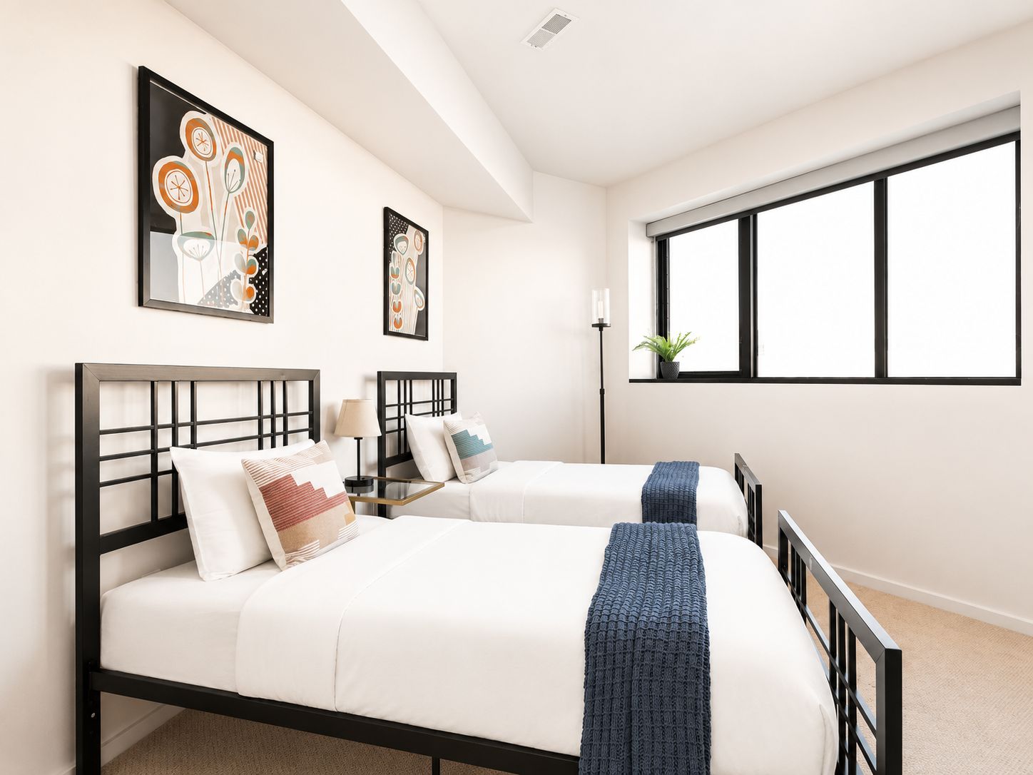 A hotel room with two beds, a large window, and artwork on the walls.