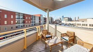 A balcony with wooden furniture and a city view. - TWO Modern Penthouses on Mass by CozySuites (Indianapolis)