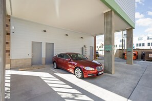Une voiture rouge est garée sous un abri-voiture, avec un bâtiment en arrière-plan.