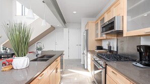 A modern kitchen with wooden cabinets, stainless steel appliances, and a large island with a sink. - TWO Modern Penthouses on Mass by CozySuites (Indianapolis)