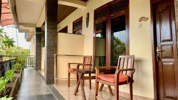 A covered outdoor seating area with two wooden chairs and a table, a door labeled "ROOM 2", and a tiled floor. - Demank House (Ubud)