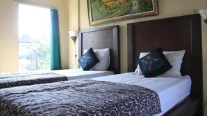 A hotel room with two beds, a large painting on the wall, and a window with curtains. - Demank House (Ubud)