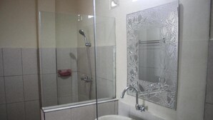A bathroom with a glass-enclosed shower, a sink, and a decorative mirror. - Demank House (Ubud)