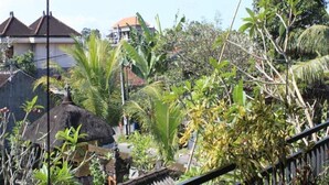 A tropical garden with a thatched-roof structure, lush greenery, and residential buildings in the background. - Demank House (Ubud)