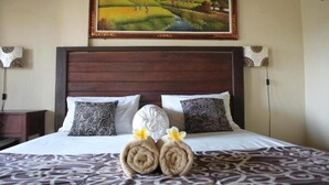A hotel room with a wooden headboard, patterned pillows, a bed with a patterned bedspread, and a painting above the bed. - Demank House (Ubud)