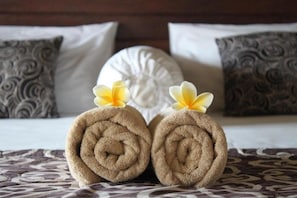 Dos toallas enrolladas con flores sobre una cama con ropa de cama estampada y almohadones decorativos.