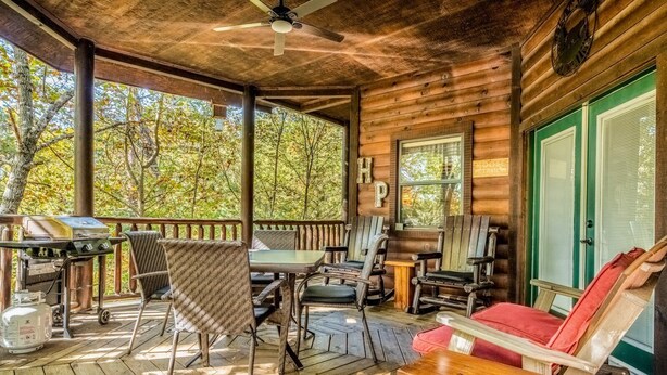 Una baita di legno con un portico, posti a sedere all'aperto, un barbecue e un orologio sulla parete.