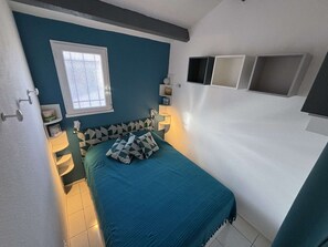Ein Schlafzimmer mit einem Bett, einem Fenster, einem Nachttisch und einem an der Wand befestigten Regal.