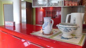 Un comptoir rouge avec une enseigne, un pichet blanc, un saladier bleu et blanc, et une étagère remplie d’ustensiles de cuisine.