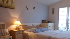 Une chambre à coucher comprenant un lit, une table de chevet, une chaise, une commode et une fenêtre avec des rideaux.