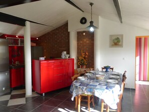 Uma sala de jantar com uma mesa posta para quatro, uma ilha de cozinha vermelha e uma parede de tijolos.