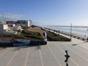 Um calçadão costeiro com piso de azulejos, uma praia e edifícios ao fundo.