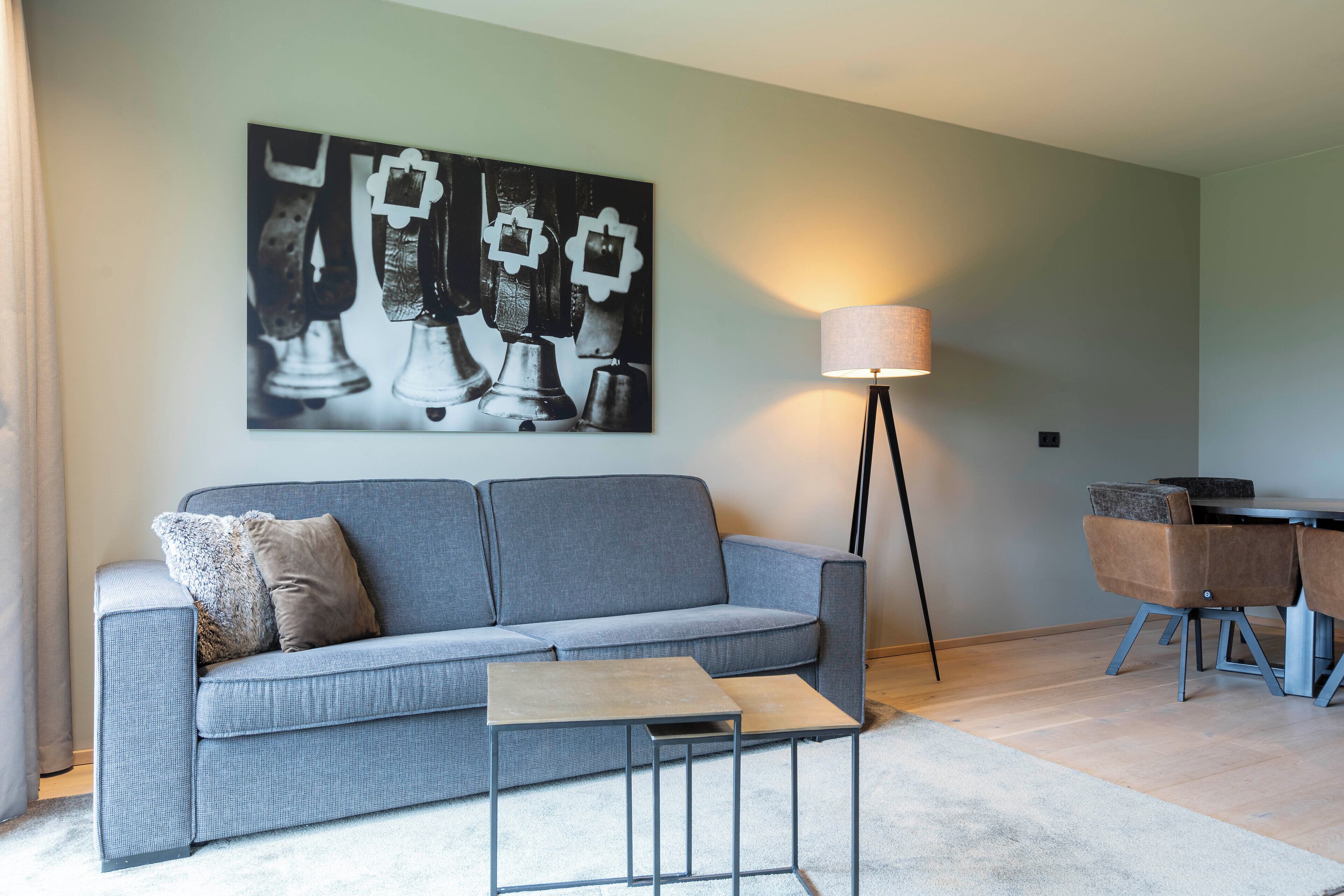 A living room with a grey sofa, a small coffee table, a floor lamp, and a dining area with chairs.