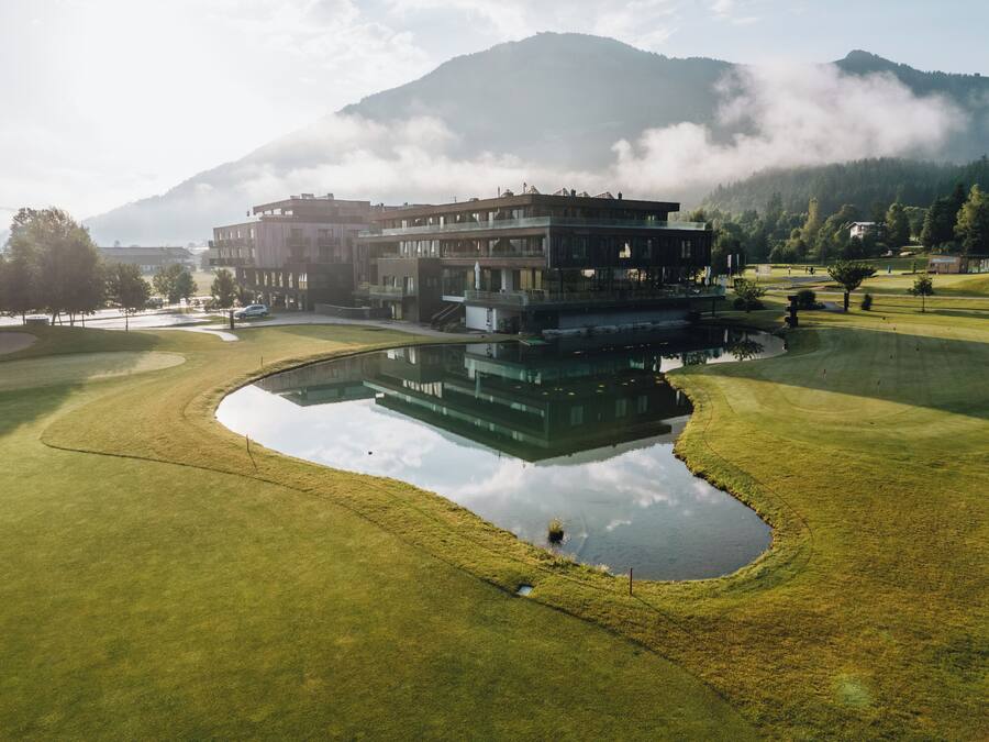 A golf course with a building complex, a pond, and mountains in the background.