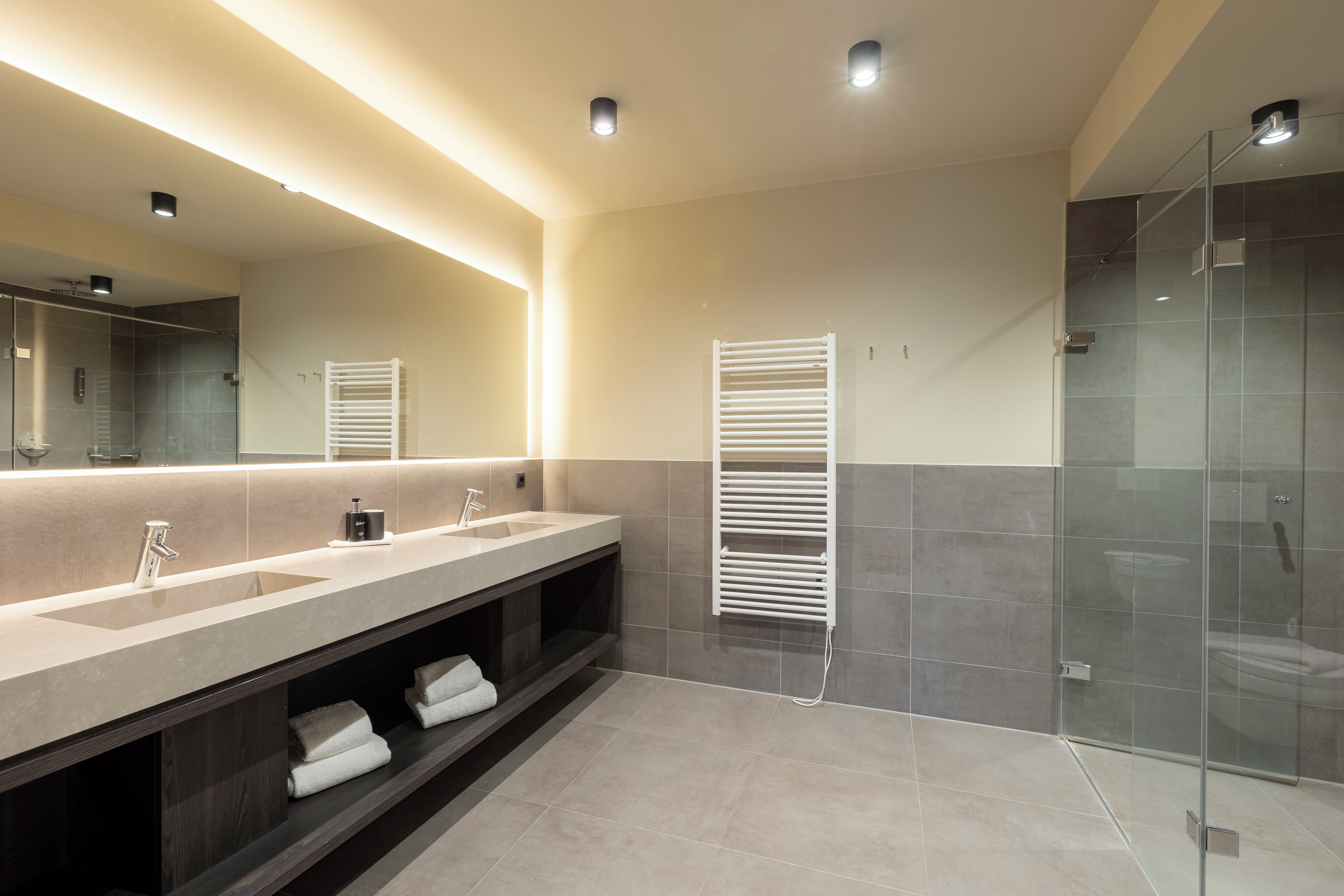 Ein modernes Badezimmer mit zwei Waschbecken, einem großen Spiegel, einer Duschkabine aus Glas und einem Handtuchhalter.