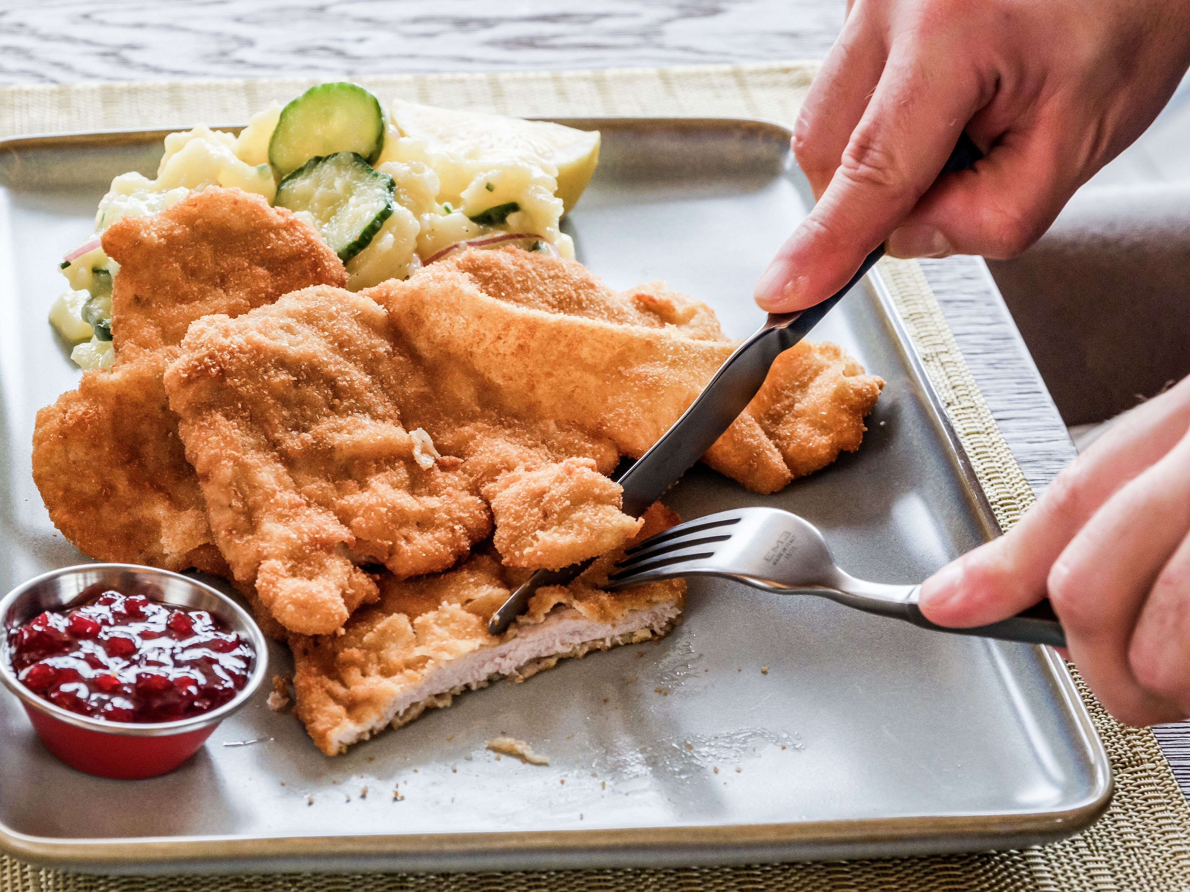 A plate of breaded cutlet, mashed potatoes, and cucumber salad with a small bowl of cranberry sauce.