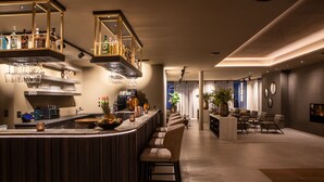 A modern bar area with a curved counter, bar stools, and shelves stocked with bottles and glasses. - Berg & Golf Resort Westendorf by ALPS RESORTS (Westendorf)