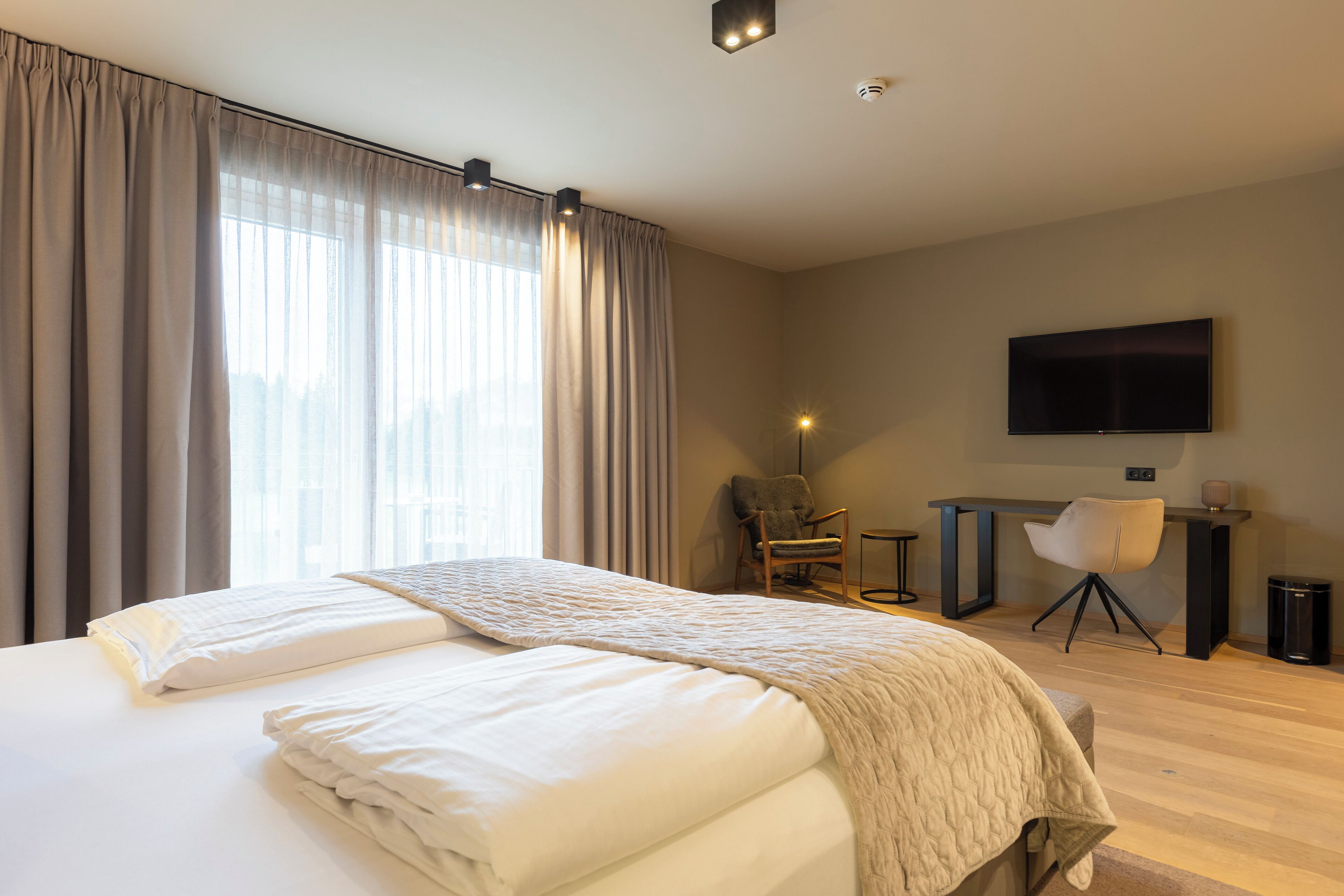 A modern hotel room with a large bed, a desk, and a TV.